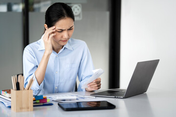 Stressed young asian employee woman calculate tax, income and expenses, looking at bills of credit card for payment or payday on table at home office.