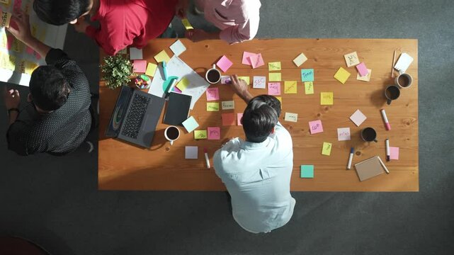 Top view of skilled business people discuss plan at meeting room while writing idea at sticky notes and stick at whiteboard. Group of diverse team working together to planning strategy. Convocation.