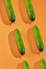 Green cucumbers on orange background arranged diagonally; ideal for food blogs, cooking websites, healthy lifestyle content, and culinarythemed designs.