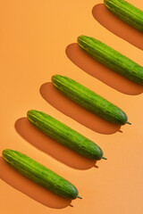 Green cucumbers on orange background arranged diagonally; ideal for food blogs, cooking websites, healthy lifestyle content, and culinarythemed designs.