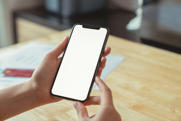 Hand holding black smartphone with blank screen on wood background.