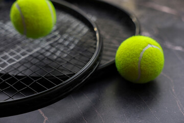 Against the background of dark marble, two tennis rackets lie one on top of the other, yellow tennis balls lie on them and next to them. The concept of sports and competitions. High quality photo