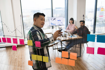 Team collaborating during brainstorming session using sticky notes and charts on glass wall in office. Team members discussing ideas, planning strategy, and analyzing data.