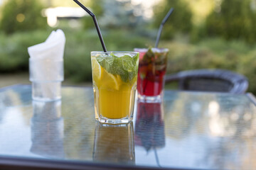 A glass of orange juice with a straw in it sits on a table next to another glass