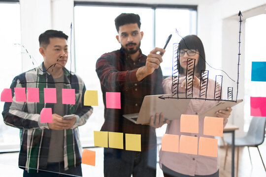 Group of professionals working together on business plan using chart drawings and sticky notes. Team brainstorming and analyzing data for project development in modern office setting.