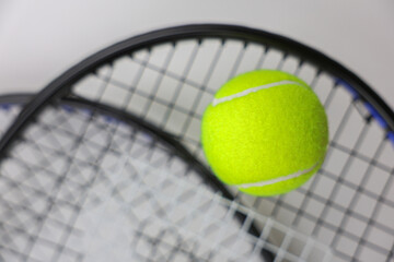 A yellow tennis ball lies against the background of two tennis rackets lying on top of each other on a white background in close-up. Concept of sports and competitions. High quality photo
