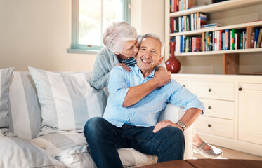 Kiss, portrait and elderly couple on sofa for connection, bonding and relaxing together at home. Smile, love and senior man and woman hugging for resting in living room at house in Switzerland.