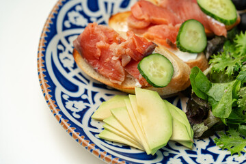 Colorful plate of smoked salmon sandwiches with cucumbers, greens, and olives on a decorative blue platter