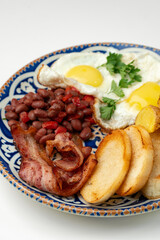 Delicious breakfast plate featuring eggs, beans, bacon, and potato wedges served on a decorative dish