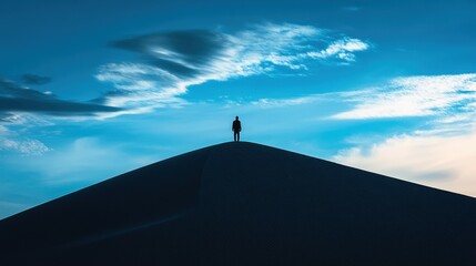 A solitary figure stands atop a silhouetted hill under a dramatic sky, capturing a moment of tranquility and reflection.
