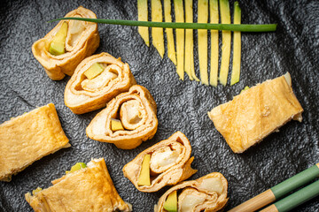 Tamagoyaki or a traditional Japanese omelet roll with avacado and cheese on a black mica plate with soy sauce and chopsticks. High quality photo
