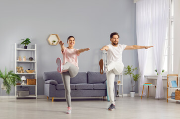 Obraz premium Happy family, husband and wife, exercises together in the living room at home, performing leg raises for stretching. They are happy to workout as a couple, promoting a healthy lifestyle.