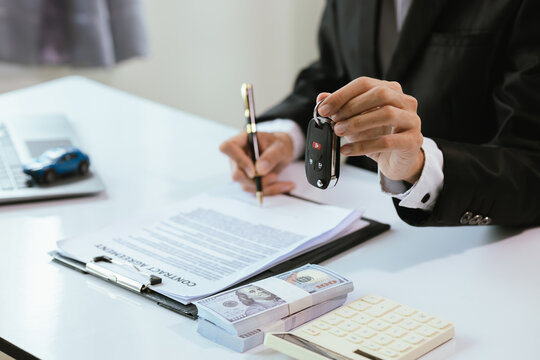 A satisfied customer signs paperwork at a car dealership, finalizing the purchase of a new vehicle. The salesman hands over the car key, completing the finance and insurance deal.