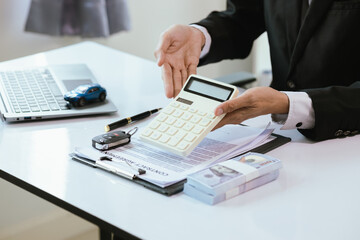 A satisfied customer signs paperwork at a car dealership, finalizing the purchase of a new vehicle. The salesman hands over the car key, completing the finance and insurance deal.