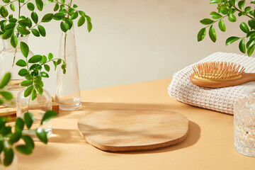 Empty wooden trays act as product placement space on the table, surrounded by glass bottles have branches next to wooden combs and towels. Minimalist spa space for promoting spa and beauty products.