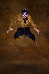 Sinister clown mid-air, eyes wide and arms outstretched, as if leaping toward his next victim against vintage dark background. Concept of Happy Halloween, party, festive mood, celebration. Ad