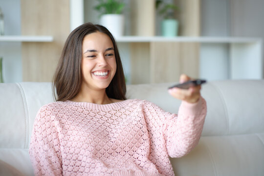 Happy woman using tv remote control at home