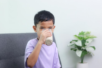 Asian little cute boy drinking milk. stays home with a smiling face, feels happy, and enjoys...