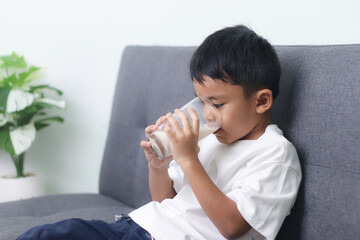 Asian little cute boy drinking milk. stays home with a smiling face, feels happy, and enjoys...