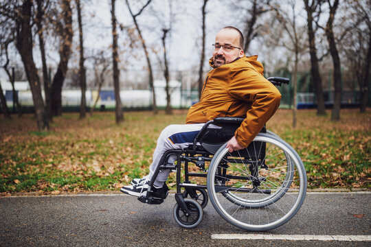 Portrait of happy paraplegic handicapped man in wheelchair in park. He is rolling on pathway.