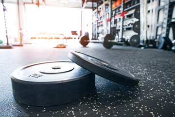 Weight plates on gym floor. Rows of gym equipment, metal barbells, dubbells on racks for strength training in gym.