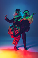Crazy, frightening clowns with furious make-up dressed vintage attire dancing in neon light against...