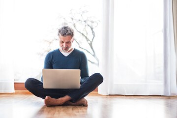 Homeoffice for handsome man. Man sitting on floor and working on laptop. Telecommuting.