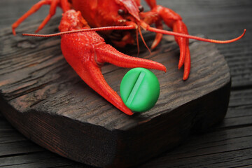 Concept, boiled red crayfish holding a green tablet in its claw, imitating an Asian mustard called wasabi. Bright red crayfish on a wooden, dark background.