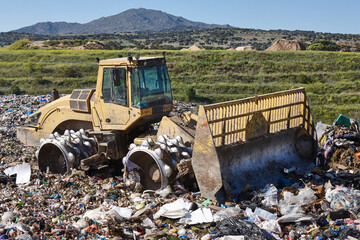 Fototapeta premium Heavy machinery shredding garbage in an open air landfill. Pollution