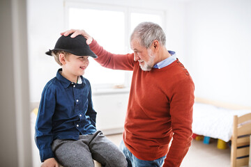 Boy is trying on grandpa's big hat, laughing. Grandfather taking care of grandson while parents are...