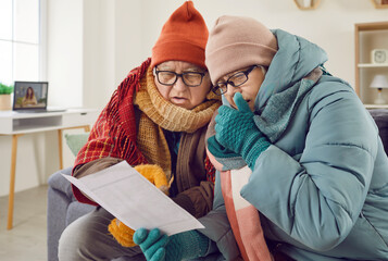 Portrait of a senior couple man and woman sitting in the living room at home in winter outerwear...