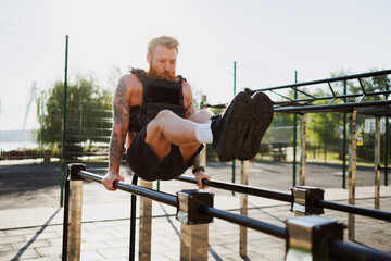 Tattooed man in weighted vest working out in outdoor gym