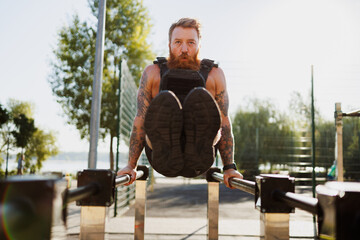 Muscular sportsman in weighted vest working out in park