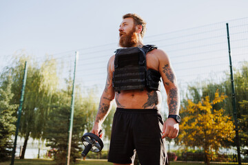 Bearded sportsman in weighted vest holding ab roller in park