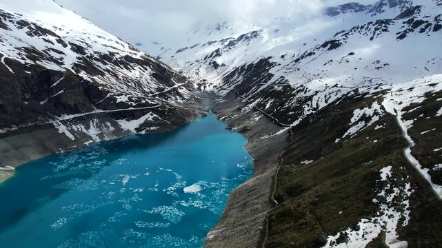 4k Drone Aerial Shot Of Vibrant Blue Glacial Water Of Lac de Moiry Dam Surrounded By Huge Mountains And Winding Trails In Grimentz Switzerland