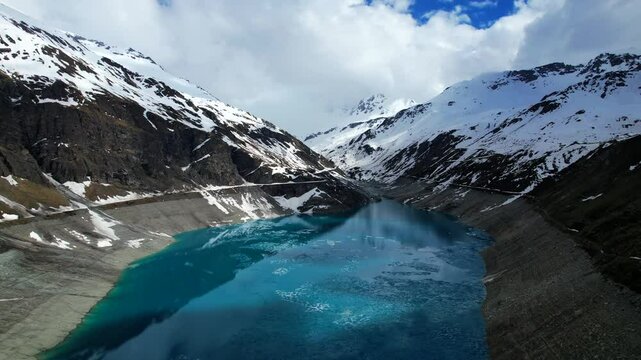 4k Drone Ascending Aerial Shot Of Vibrant Blue Glacial Water Of Lac de Moiry Dam Surrounded By Massive Snow Covered Mountains Reflecting On lake In Grimentz Switzerland