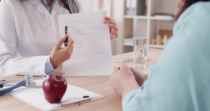 Female doctor nutritionist giving consultation to overweight fat patient woman sitting at desk in medical clinic in office about healthy nutrition and showing diet plan for weight loss. 4k video.