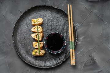 Tamagoyaki or traditional Japanese omelette with avocado and cheese on a black mica plate with soy sauce and chopsticks. Place for text. Copyspace. High quality photo