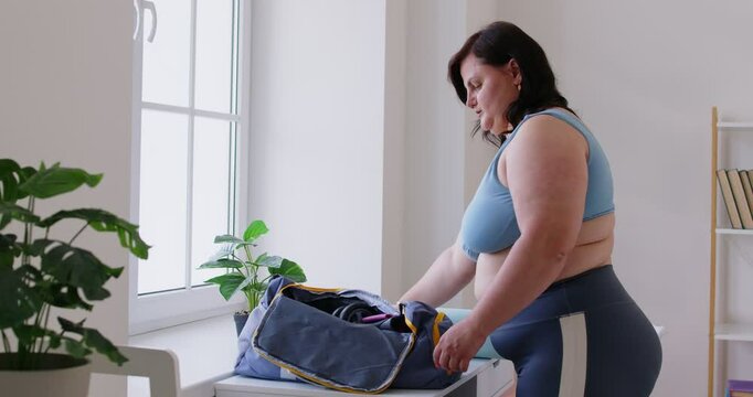 A young overweight woman in sportswear is preparing for a workout, close-up. A plus size woman puts dumbbells in a bag. Concept generative, healthy lifestyle, losing weight, sport