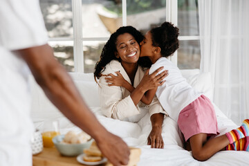 Young daughter kissing mother during breakfast in bed