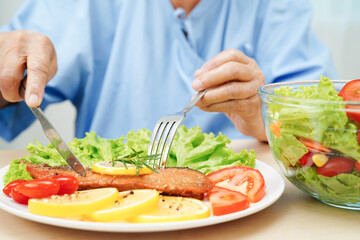 Asian elderly woman patient eating salmon stake and vegetable salad for healthy food in hospital.