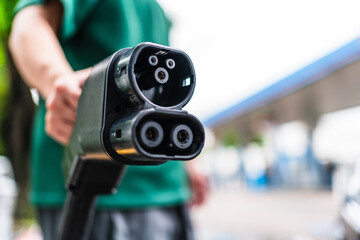 Closeup a hand holding electric vehicle DC charger plug in the outdoor energy station area. EV car...