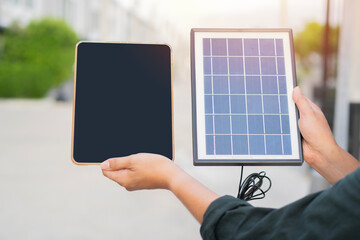 Portable solar panel connected to tablet isolated dark screen color on man hands over city park background