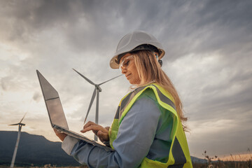 A skilled female engineer is conducting vital research at a modern wind farm, using advanced...