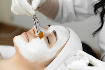 Indulge in a luxurious facial treatment at a spa, where a beautician applies a white face mask for...