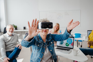 Group of seniors with VR goggles on computer and technology education class. Elderly people learning about virtual reality, using VR headset.