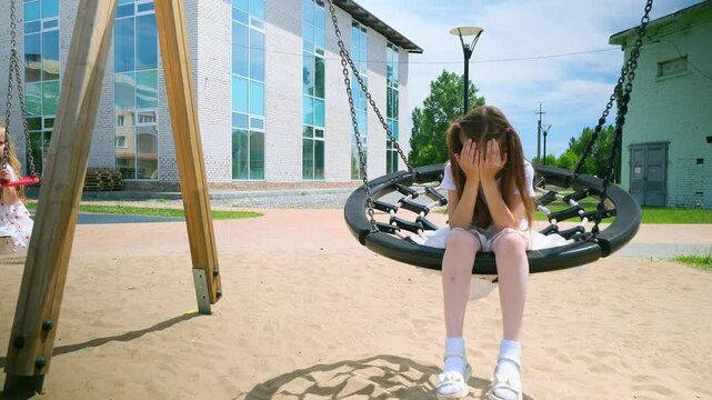 Upset ittle girl kid swinging on net swing in the park. Caucasian child swinging on playground. Cute child have saddnes in park. School girl play on swing. Slow motion