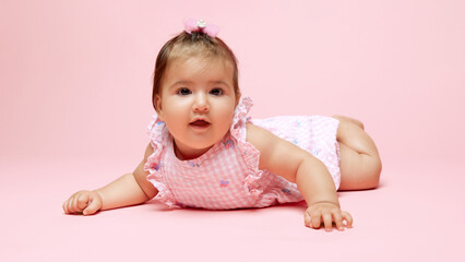 Little cute little princess exploring world, dressed in pink romper with matching bow against soft pink background. Concept of beauty, parenthood, childhood, life and birth.