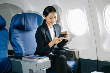 Young Asian executive excels in first class, multitasking with digital tablet, laptop and...