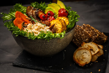 Buddha bowl with vegetables, healthy salad with avocado, carrots, corn and rice, baked chicken breast on a black background. Healthy eating concept. Copyspace. High quality photo